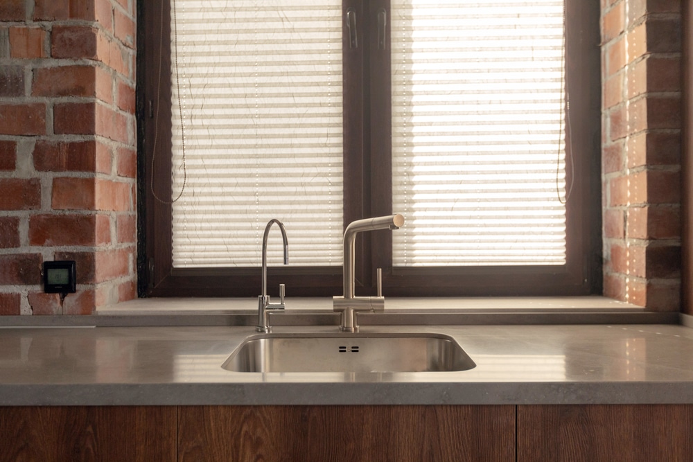 kitchen sink in front of window with light colored countertops